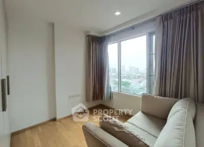 Bright living room with large window offering stunning city views, featuring cozy seating and elegant curtains.