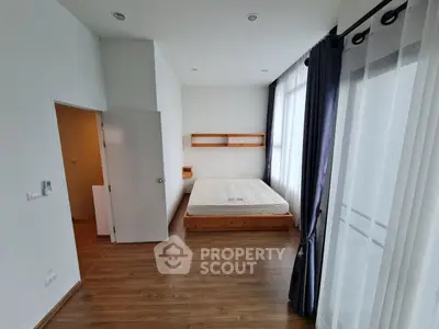 Spacious bedroom with wooden flooring and large windows for natural light.