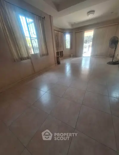 Spacious living room with large windows and tiled flooring, offering ample natural light and open space.