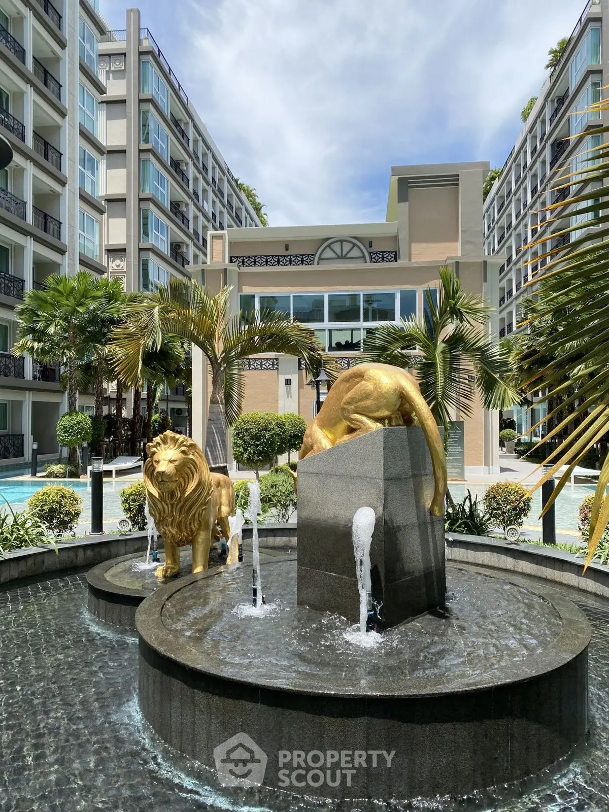 Luxurious apartment complex with elegant fountain and golden lion statues, surrounded by lush greenery.