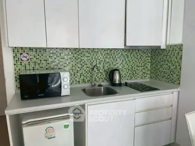 Modern kitchen with green mosaic backsplash, sleek white cabinets, and compact appliances.