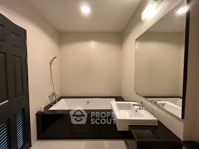 Modern bathroom with sleek black and white design featuring a bathtub and large mirror.