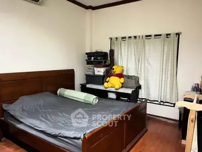 Cozy bedroom with wooden flooring and large bed, featuring a playful teddy bear and ample natural light.