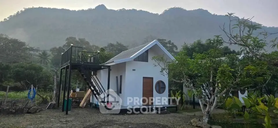 Charming small white house with mountain backdrop and elevated deck, perfect for nature lovers.