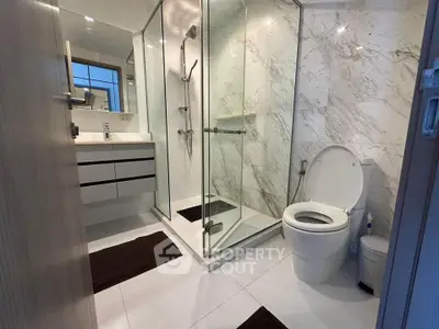 Modern bathroom with glass shower and marble walls, featuring sleek fixtures and contemporary design.