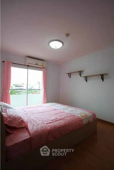 Cozy bedroom with pink decor and natural light from large window.