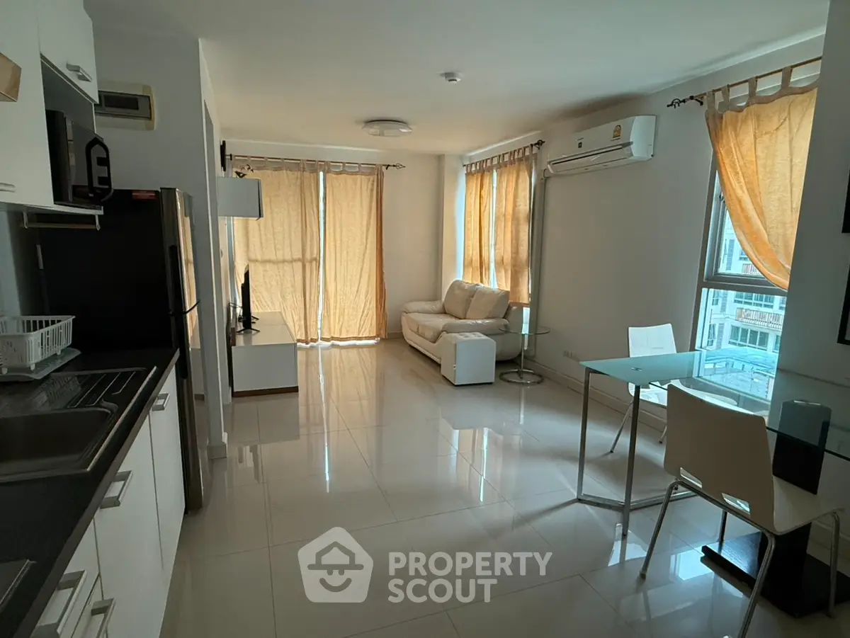 Modern open-layout living room with kitchen, featuring sleek furniture and large windows for natural light.