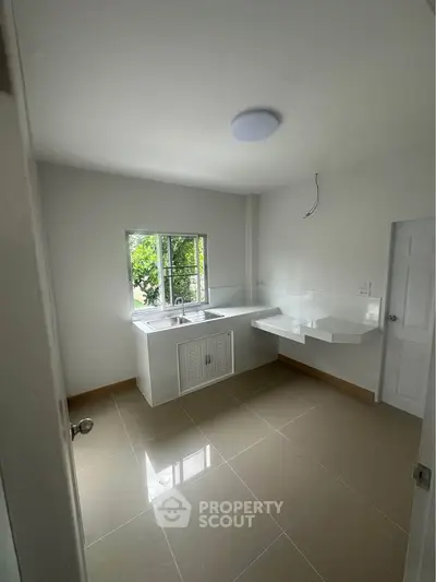 Modern minimalist kitchen with sleek white countertops and natural light from window.