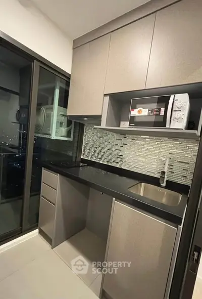Modern kitchen with sleek cabinetry and city view window, featuring a microwave and stylish backsplash.