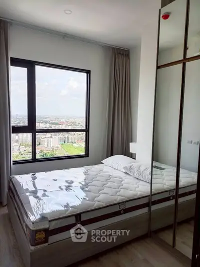 Modern bedroom with large window offering stunning city view, featuring a comfortable bed and mirrored wardrobe.