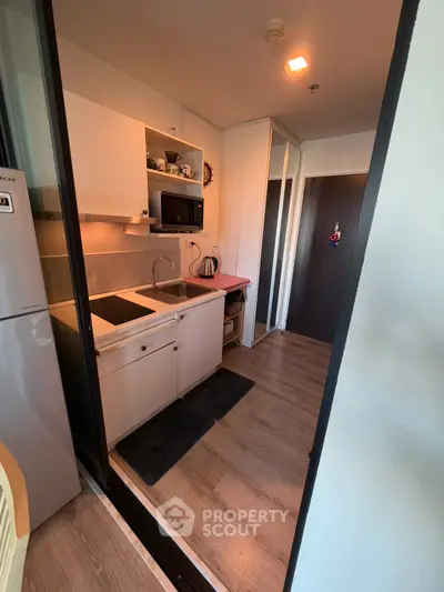 Compact kitchen with modern appliances and wooden flooring in cozy apartment