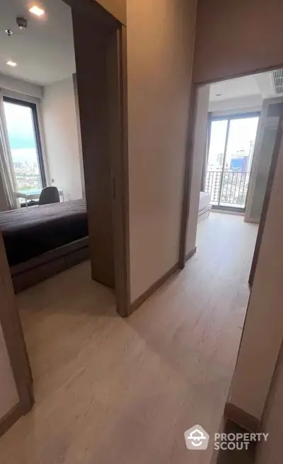 Modern apartment hallway with wooden flooring and city view from bedroom window.