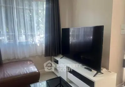 Cozy living room with modern TV setup and natural light through large window.