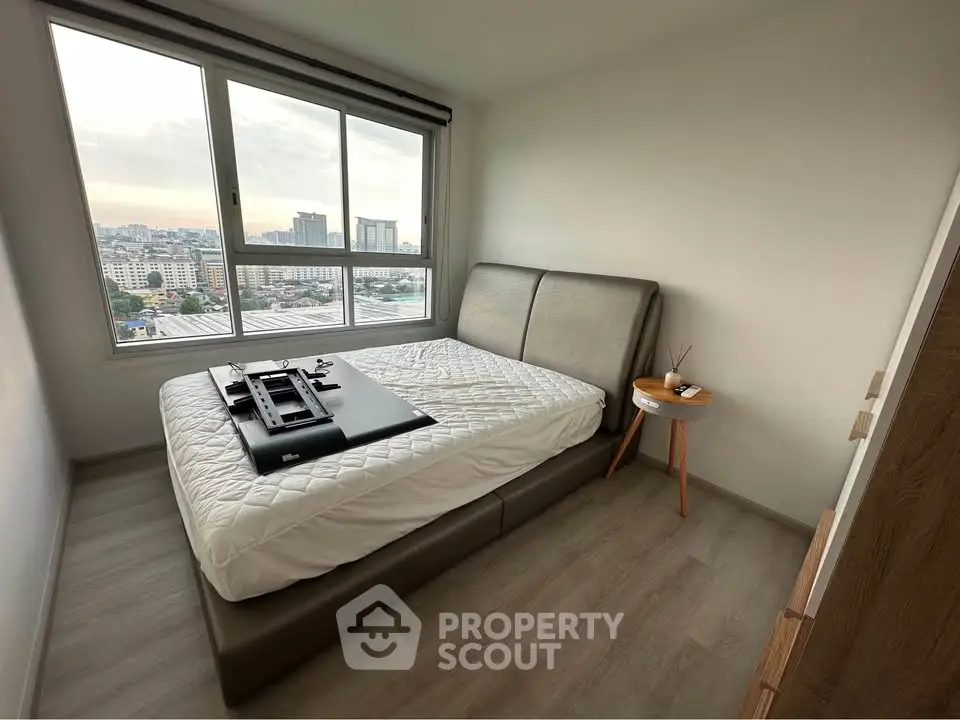 Modern bedroom with large window offering city views, featuring a stylish bed and minimalist decor.