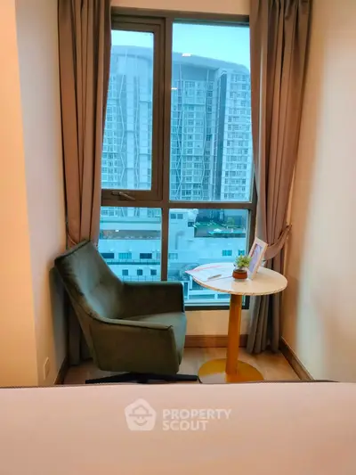 Cozy bedroom with city view, featuring a stylish chair and table by the window.