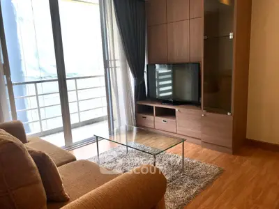 Modern living room with glass coffee table and large TV, featuring floor-to-ceiling windows and wooden flooring.