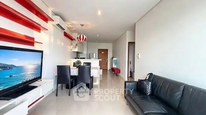 Modern living room with sleek furniture and open kitchen layout, featuring a large TV and stylish red accents.