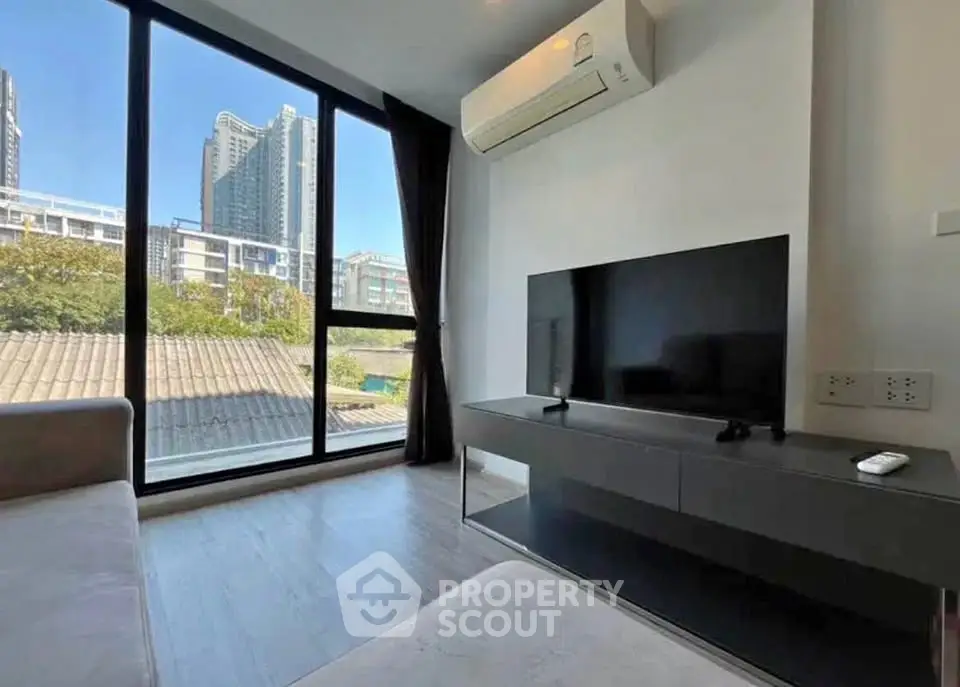 Modern living room with large window and city view, featuring sleek furniture and air conditioning.