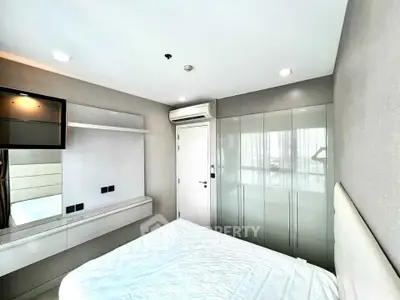 Modern bedroom with sleek built-in wardrobe and wall-mounted TV, featuring minimalist design and ample natural light.
