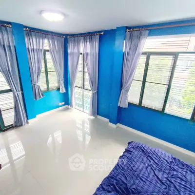 Spacious bedroom with vibrant blue walls and large windows offering natural light.