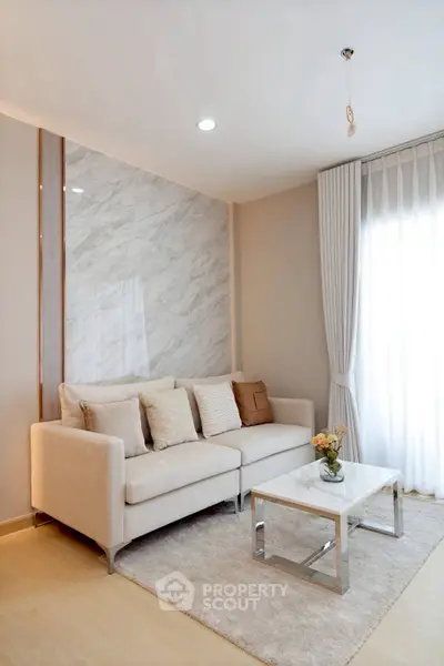Elegant living room with modern sofa, marble accent wall, and natural light from large window.
