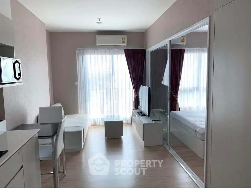 Modern apartment interior with open living room and bedroom, featuring sleek furniture and natural light.