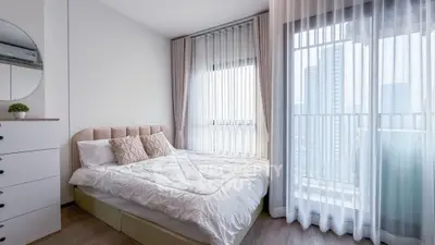 Bright modern bedroom with large windows and city view, featuring elegant decor and cozy bedding.