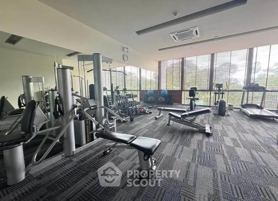 Spacious gym with modern equipment and large windows offering natural light.