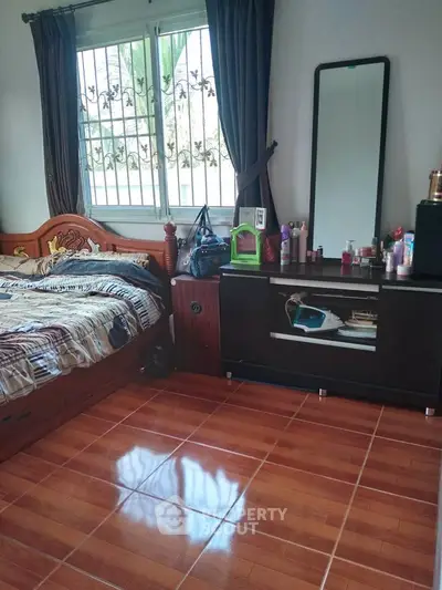 Cozy bedroom with wooden flooring and elegant decor, featuring a large mirror and ample natural light.