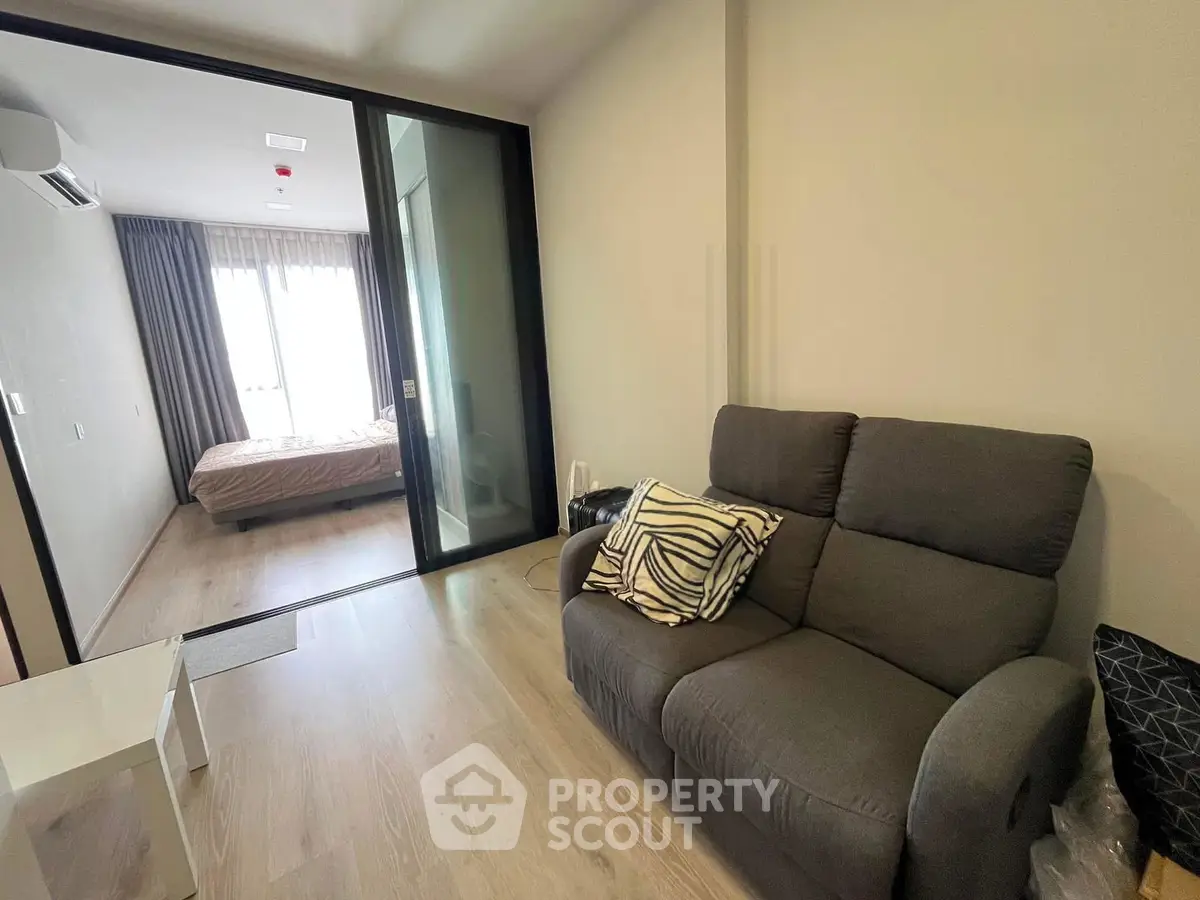 Modern apartment interior with cozy living room and bedroom separated by glass doors.