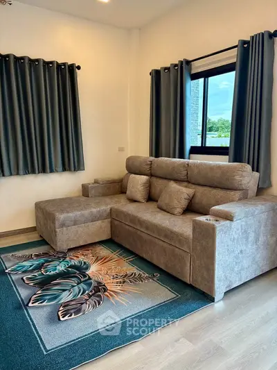 Modern living room with plush gray sofa and stylish rug, featuring large windows with elegant curtains.