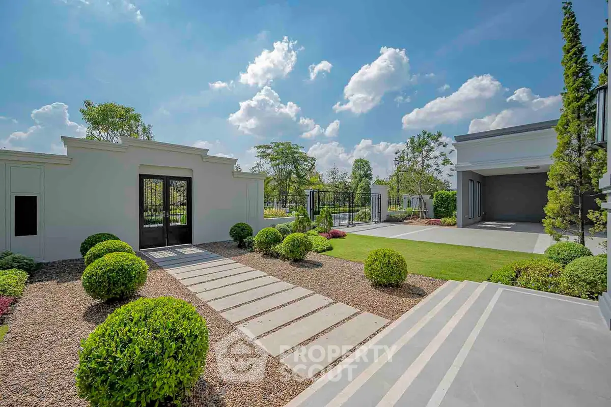 Luxurious modern home exterior with manicured garden and spacious driveway under a clear blue sky.