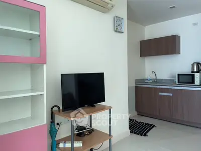 Modern compact living room with kitchenette, featuring TV, microwave, and stylish shelving unit.