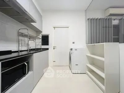 Modern kitchen with sleek appliances and ample storage space, featuring a washing machine and microwave.