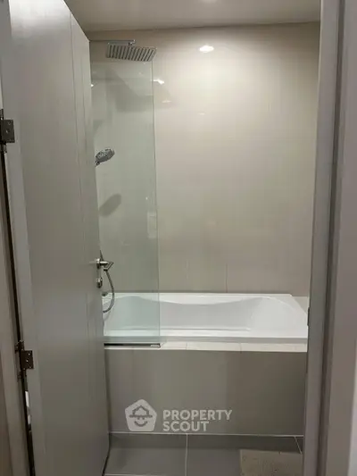 Modern bathroom with sleek bathtub and glass shower partition in contemporary apartment.