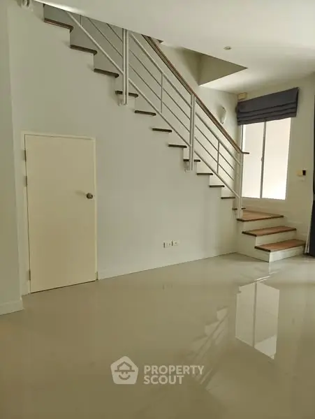 Modern interior with sleek staircase and glossy tiled floor, ample natural light from large window.