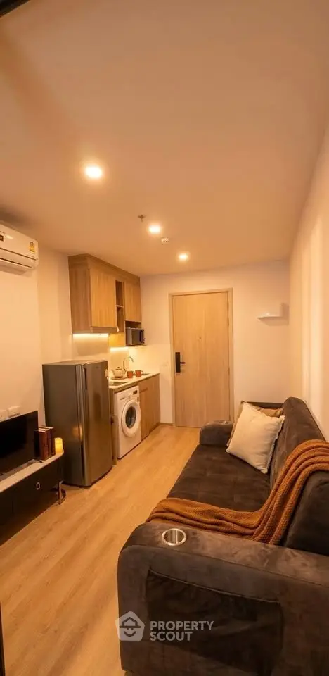 Cozy modern living room with kitchen, featuring a plush sofa, washing machine, and sleek appliances.