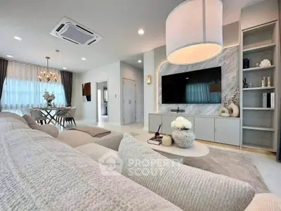 Luxurious modern living room with elegant decor and open dining area, featuring a large TV and stylish lighting.