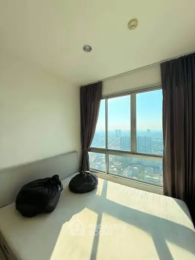 Bright bedroom with large window offering stunning city view, perfect for urban living.