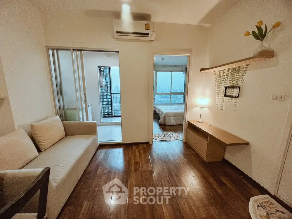 Cozy living room with wooden flooring and modern decor, leading to a bright bedroom with city views.