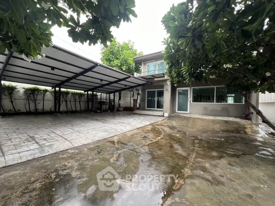 Spacious modern home with large driveway and covered parking area, surrounded by lush greenery.