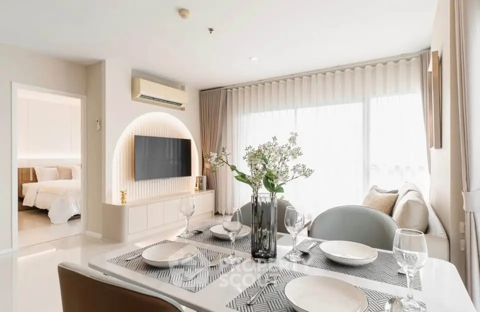 Modern living room with dining area, featuring elegant decor and natural light, adjacent to a cozy bedroom.