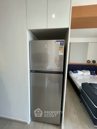 Modern apartment interior with sleek fridge and cozy bedroom view