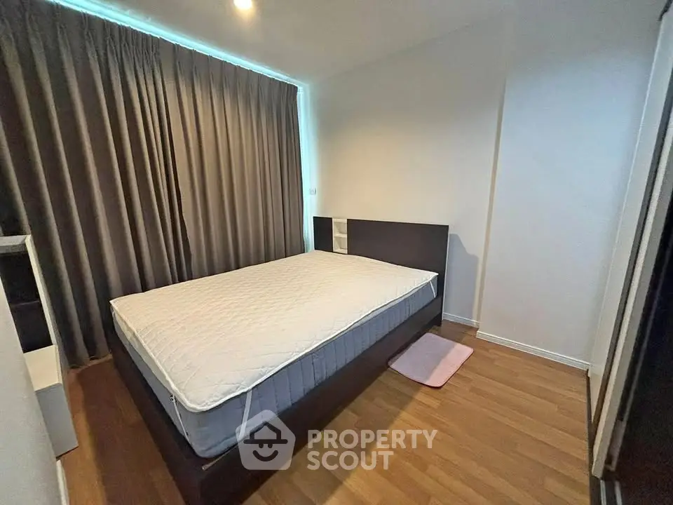 Cozy bedroom with wooden flooring and large window with curtains, perfect for relaxation.