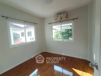 Bright empty room with wooden flooring and large windows in a modern home.