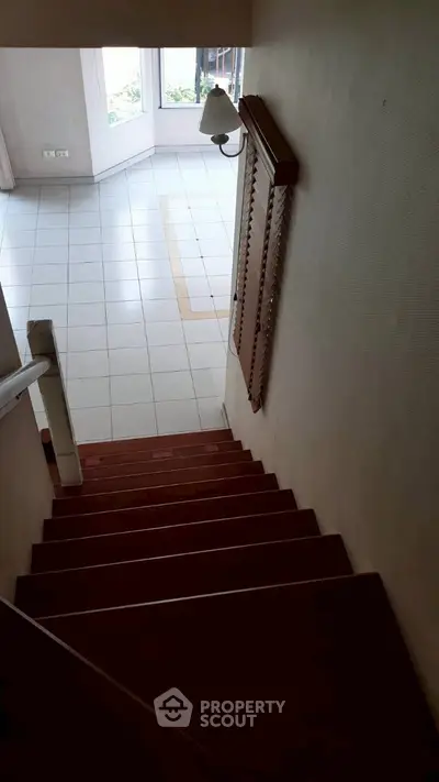 Spacious home interior with wooden staircase leading to a bright tiled living area.