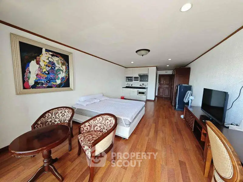 Spacious studio apartment with modern furnishings and hardwood floors, featuring a cozy seating area and a compact kitchen.