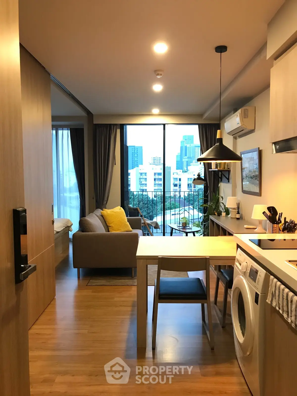 Modern apartment with open kitchen and city view, featuring cozy living area and washing machine.