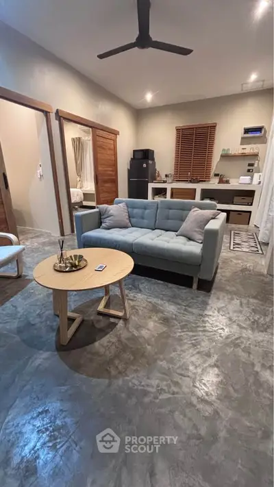 Modern living room with stylish decor and polished concrete floor, featuring a cozy sofa and sleek ceiling fan.