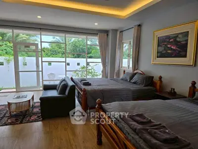 Spacious bedroom with large windows and garden view, featuring elegant decor and cozy seating area.